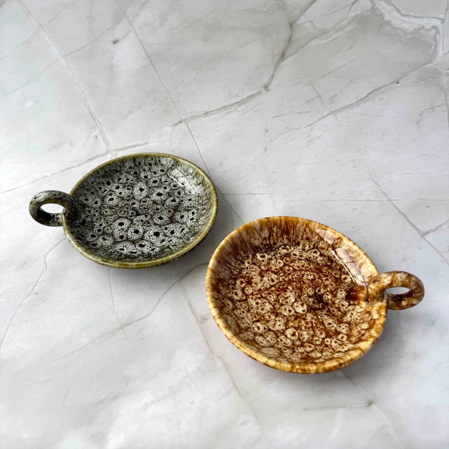 Two ceramic bowls with speckled glaze on a textured white surface