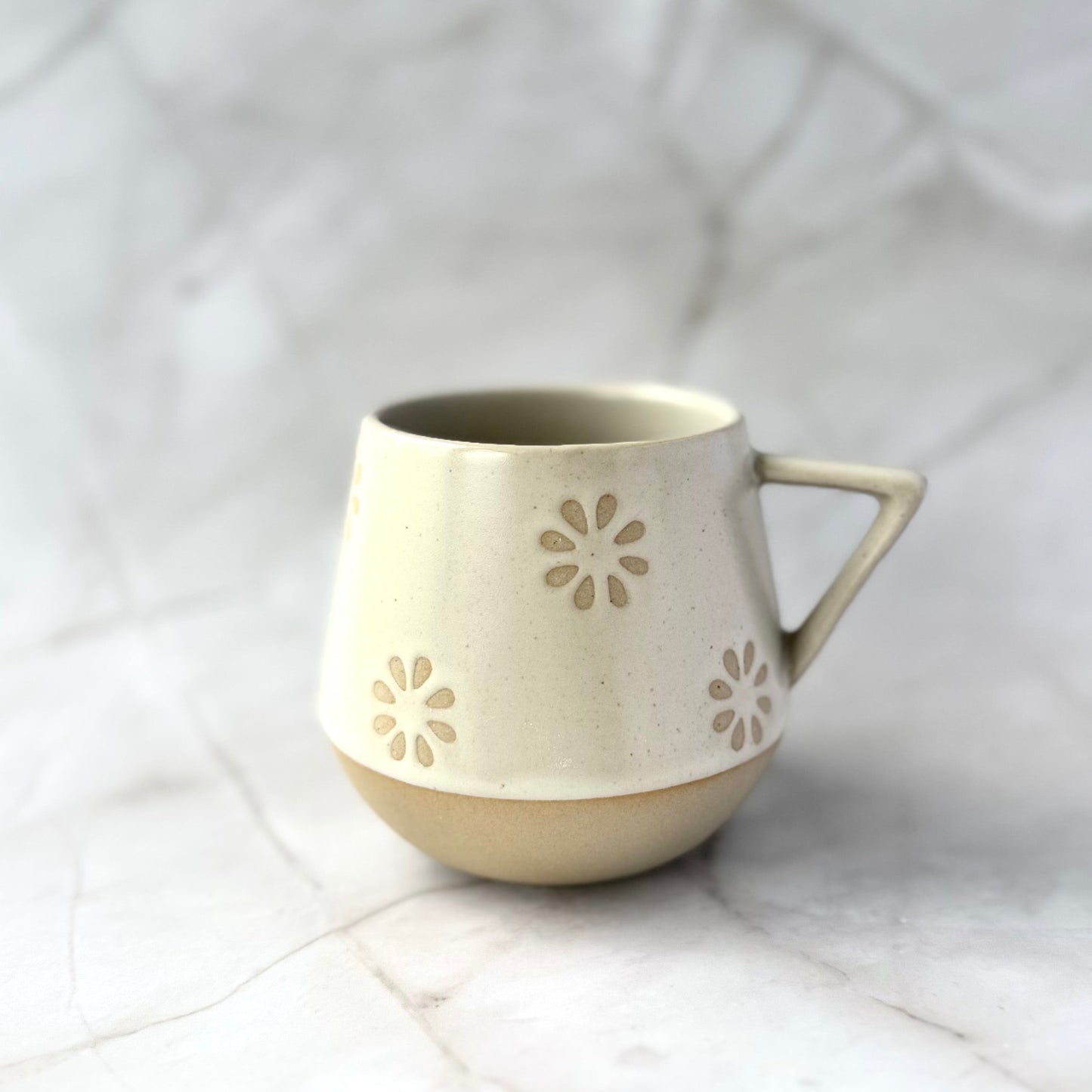 Warm beige and soft white with natural brown undertones ceramic mug with floral patterns on a white textured surface