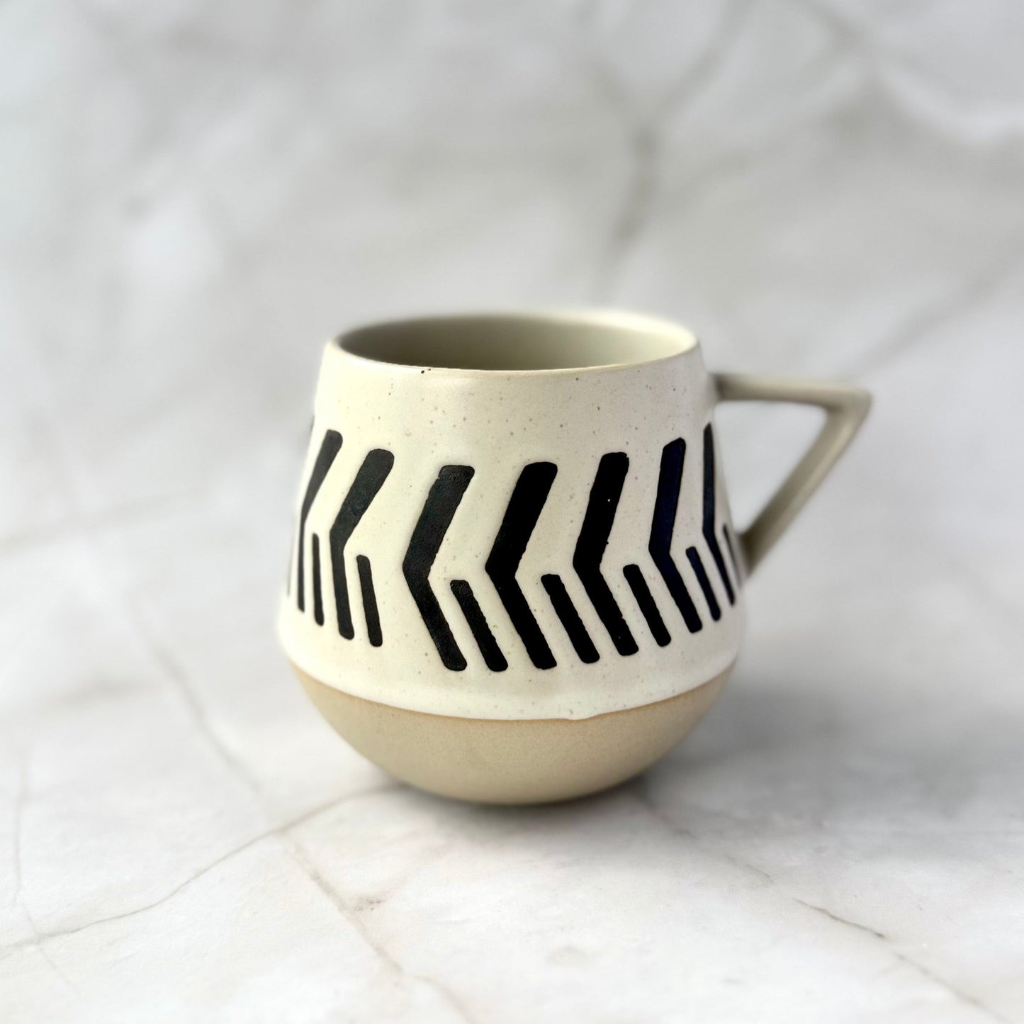 warm beige and soft white with natural brown undertones ceramic mug with black arrrow pattern on a white marble surface