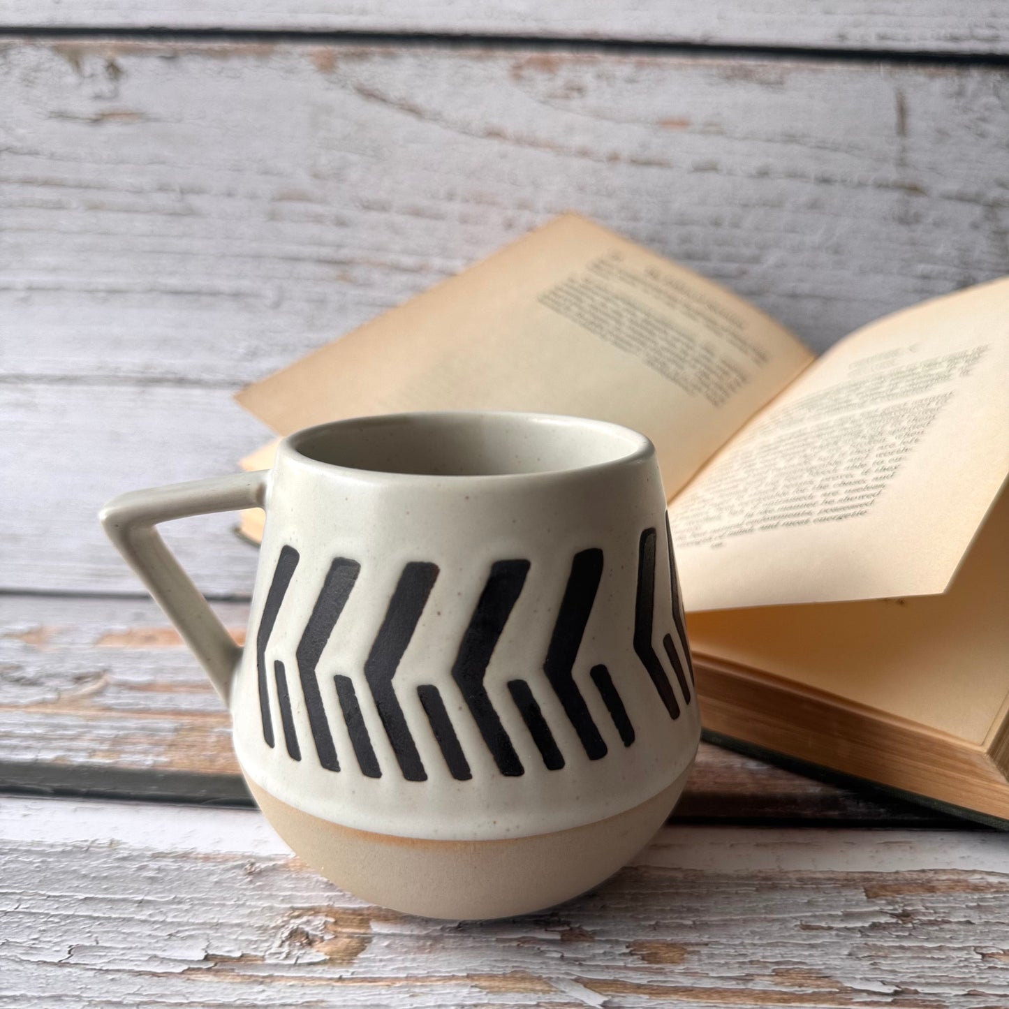 warm beige and soft white with natural brown undertones ceramic mug with black pattern on a wooden surface with an open book