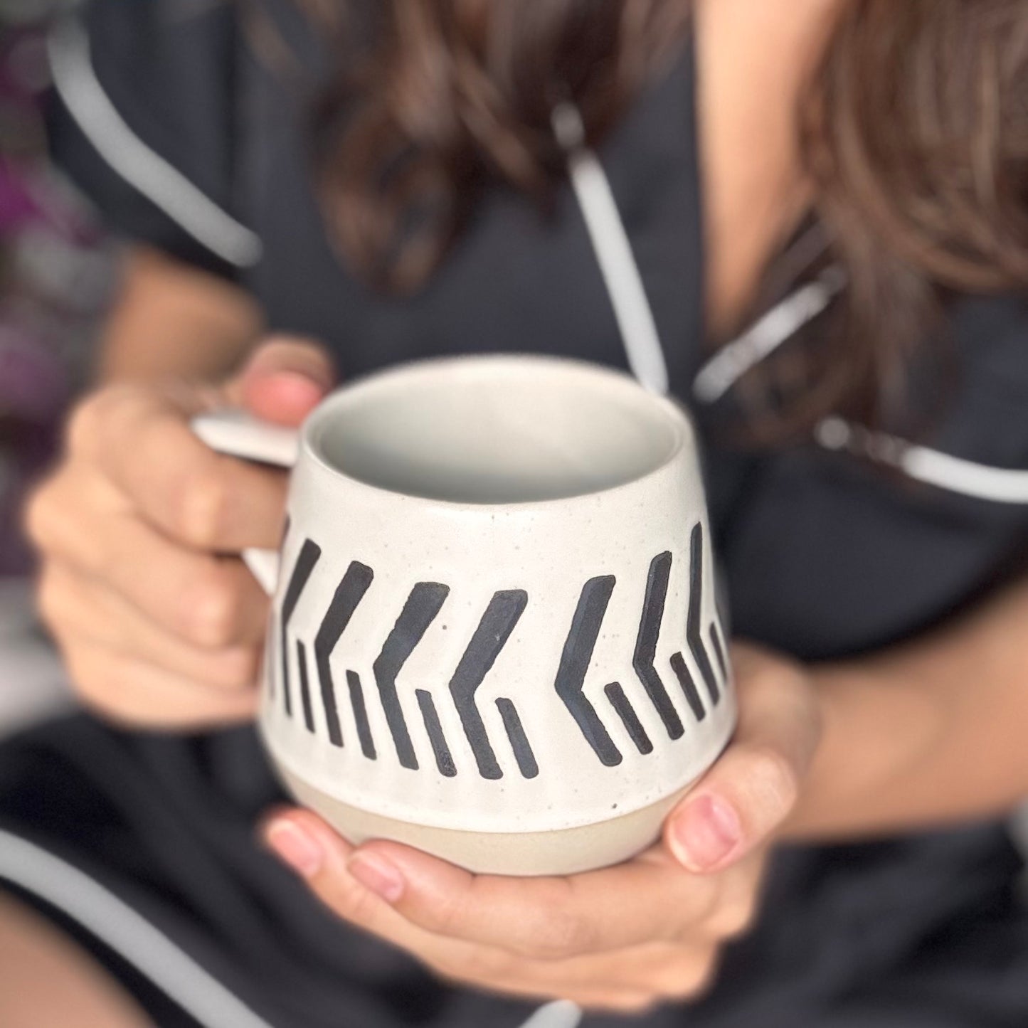 Person holding a warm beige and soft white with natural brown undertones ceramic mug with black zigzag pattern