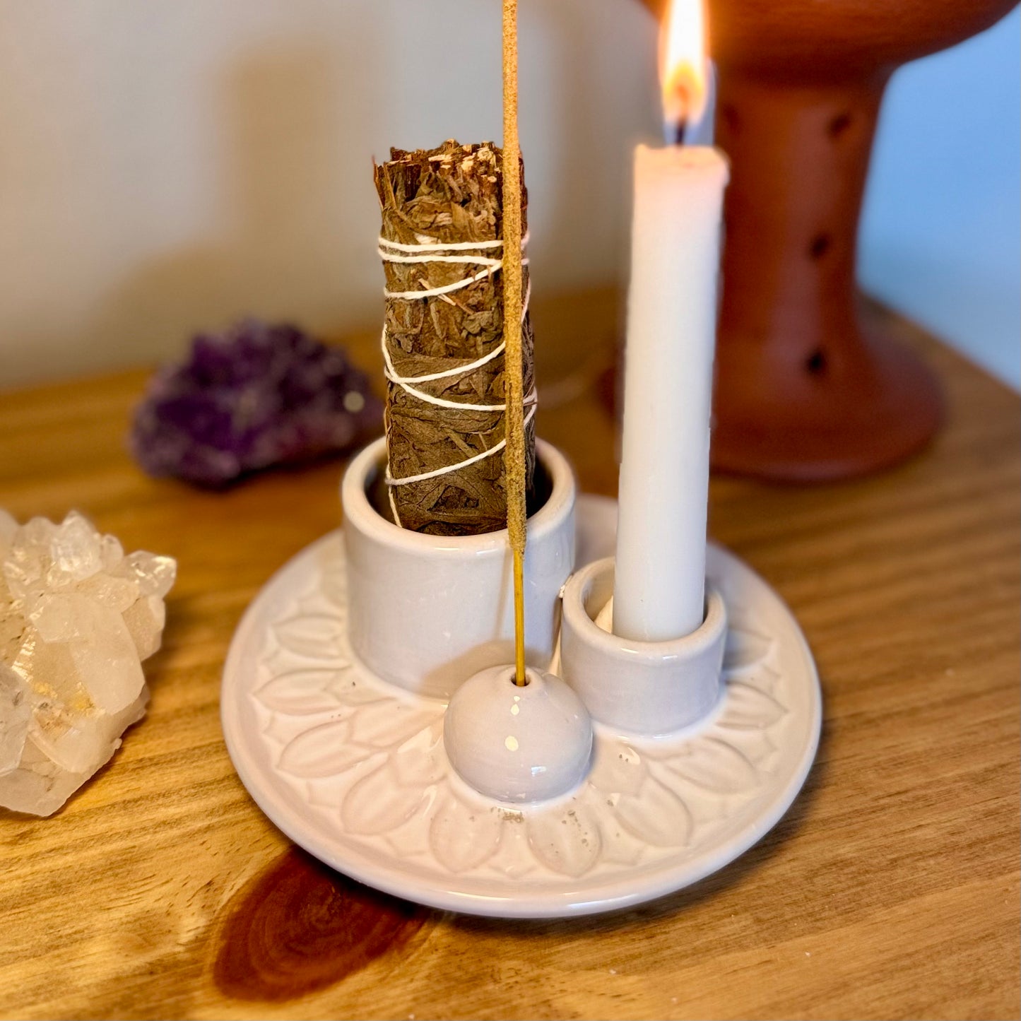 Candle and smudge stick on a decorative stand with crystals in the background