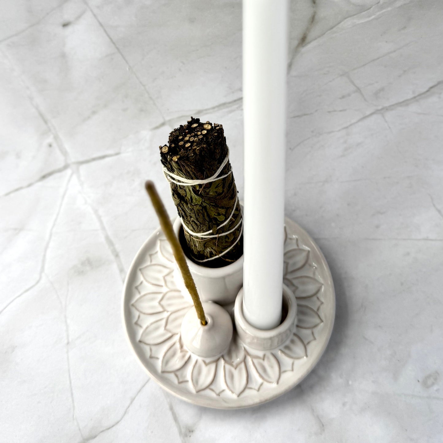 White candle and incense stick on a decorative holder against a marble background