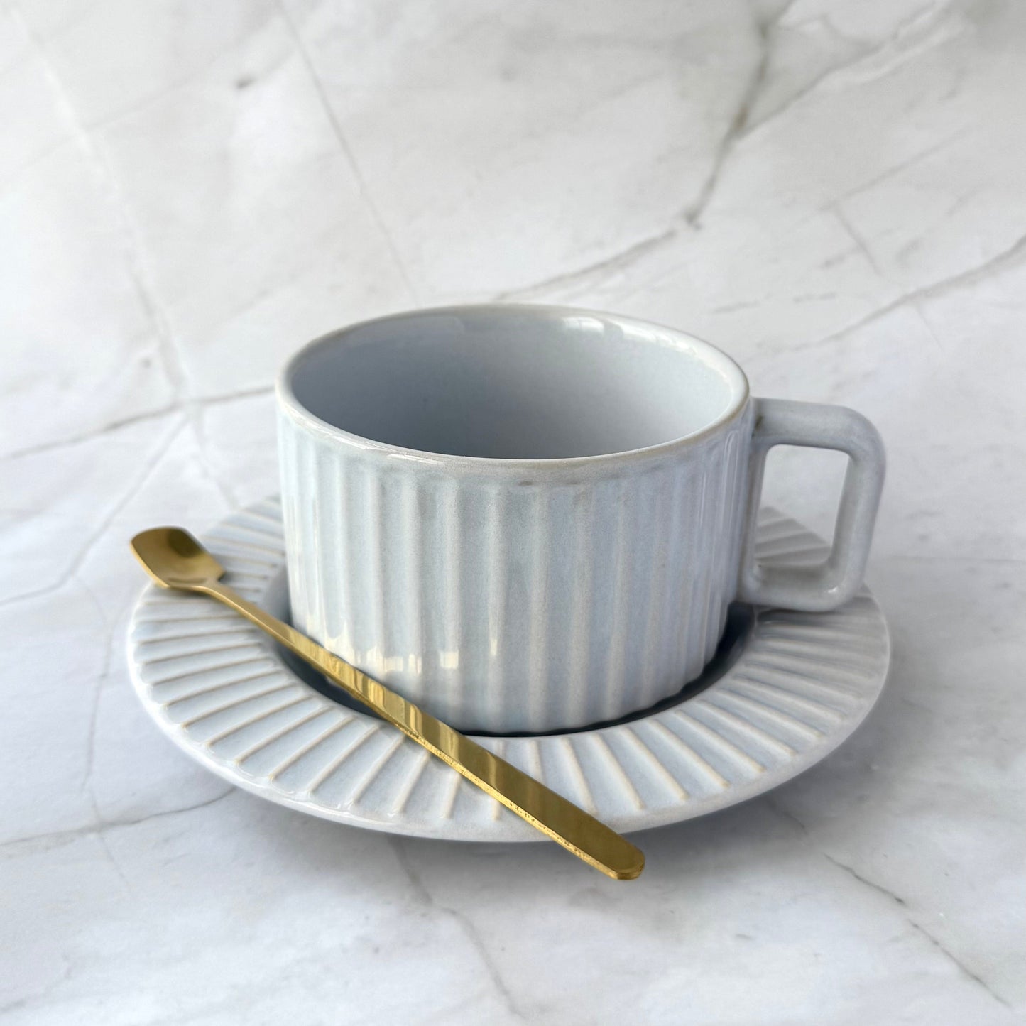 Calming light gray glaze with soft blue undertonescup with plate and gold spoon on a marble surface