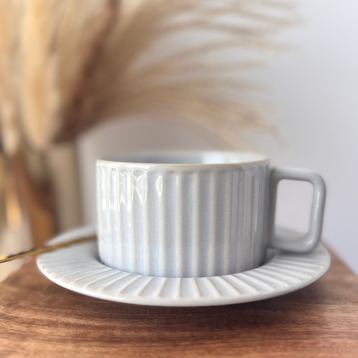Calming light gray glaze with soft blue undertones ceramic cup and saucer on a wooden surface with a blurred background