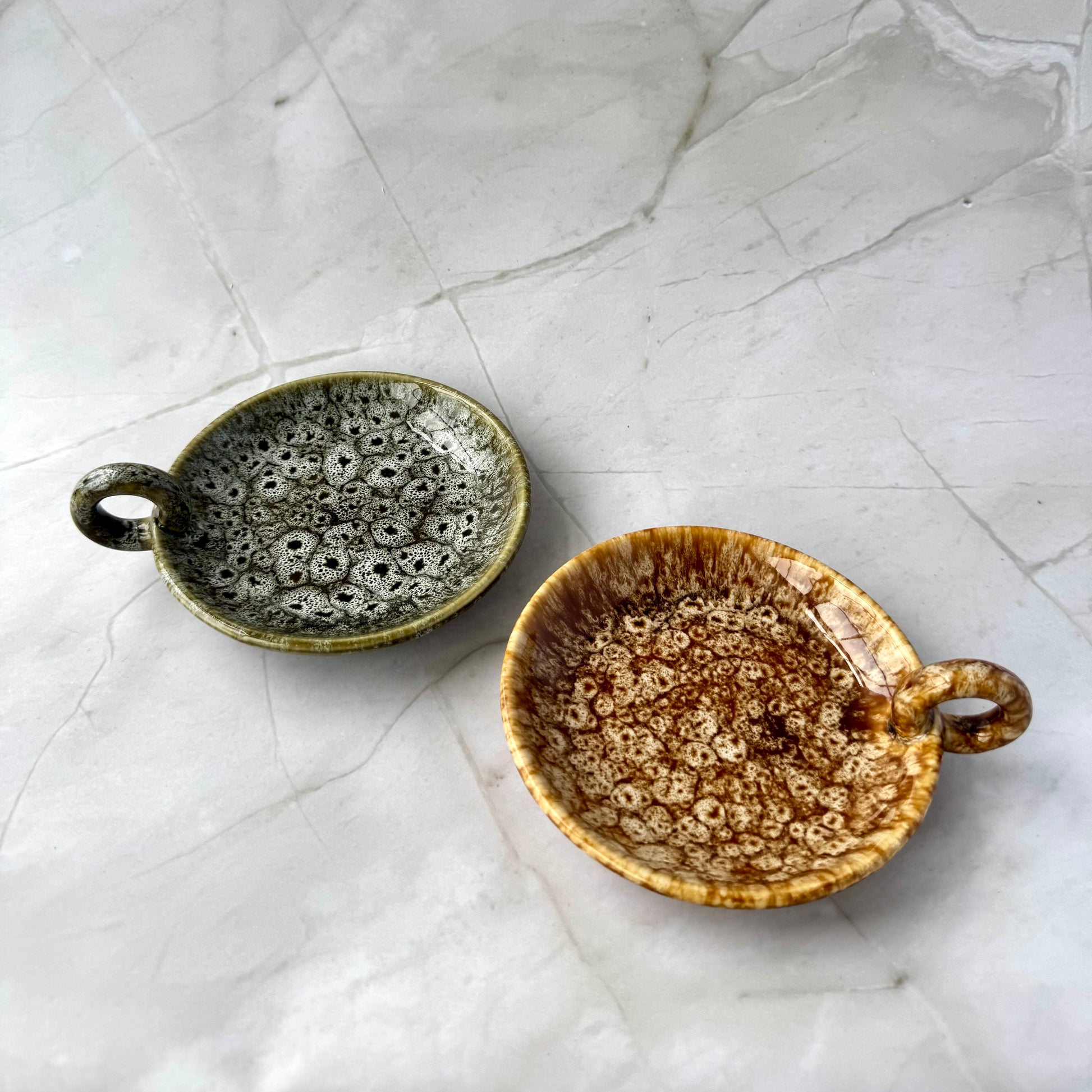 Two ceramic bowls with speckled glaze on a textured white surface