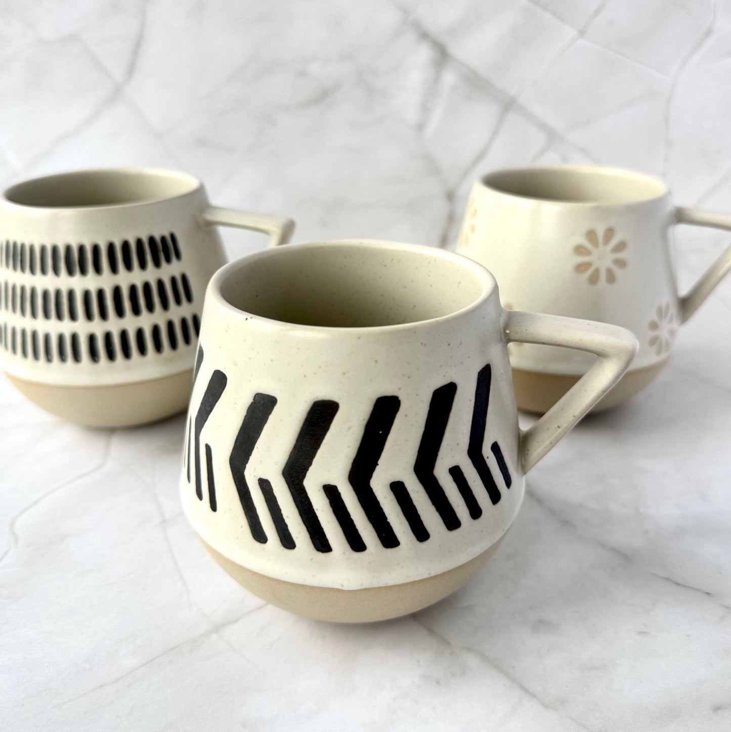 Three ceramic mugs with warm beige and soft white with natural brown undertones patterns on a white textured surface