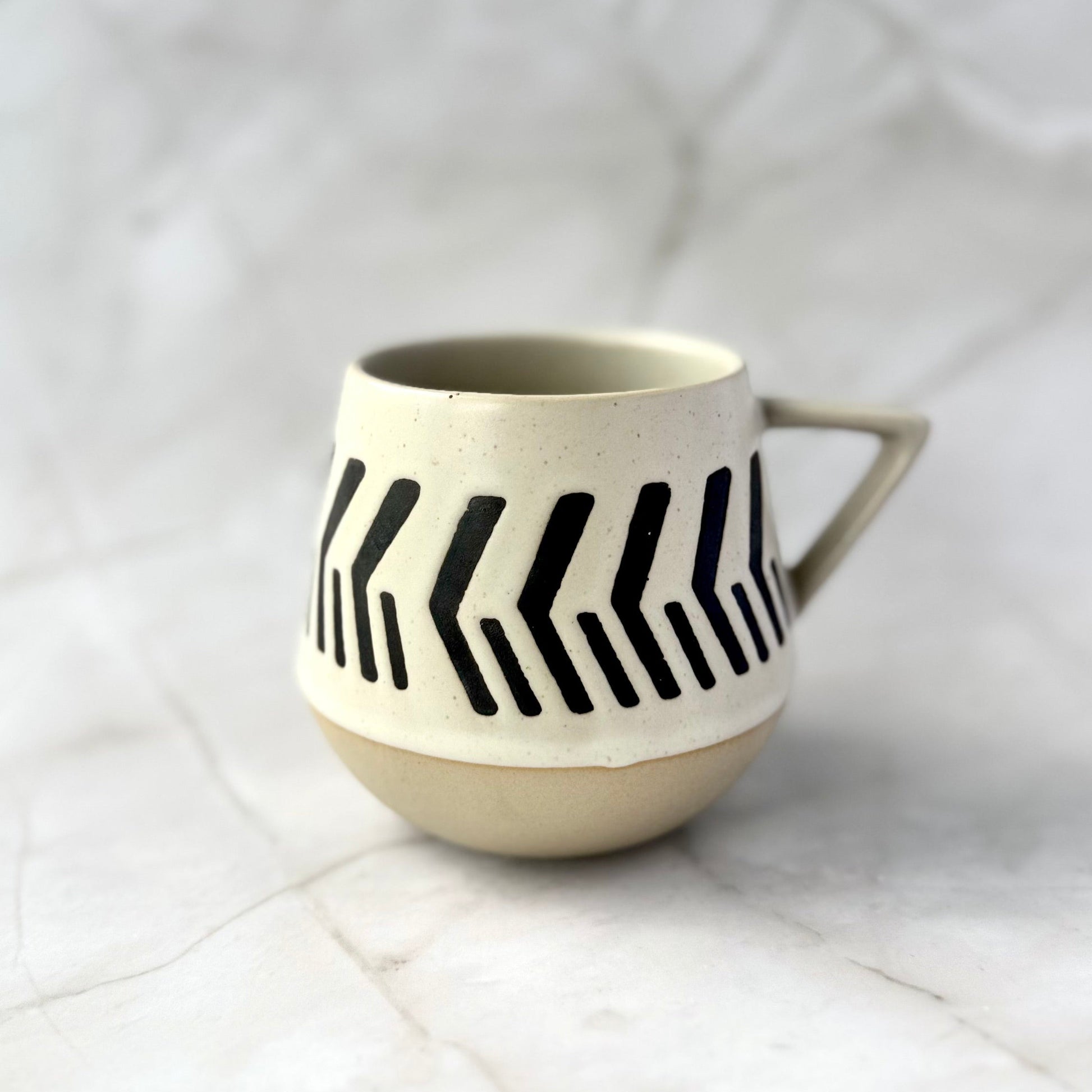 warm beige and soft white with natural brown undertones ceramic mug with black arrrow pattern on a white marble surface