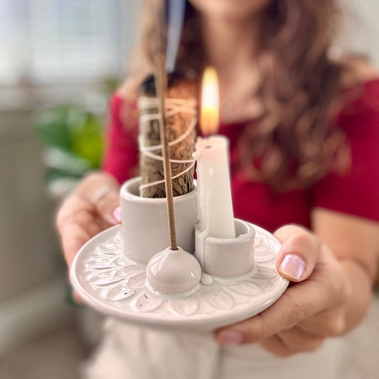 Person holding a white ceramic candle holder with a lit candle and decorative elements.