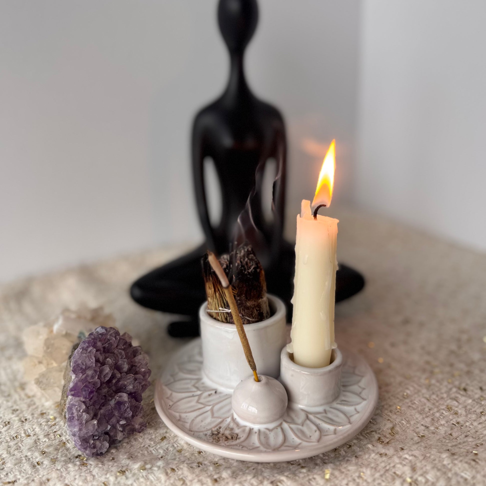 Candle and incense stick on a decorative stand with a black abstract sculpture and amethyst crystal in the background.